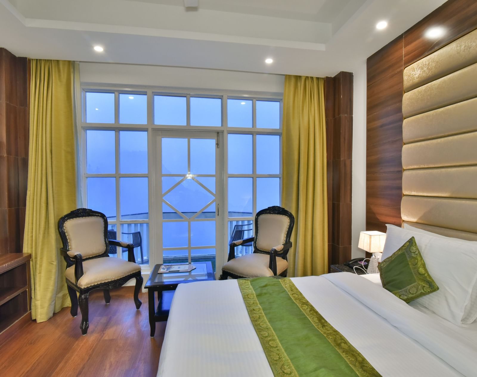 A large bed next to two chairs placed near a large window in the Premium Room at DLS Highland Resort and Spa, Mussoorie.